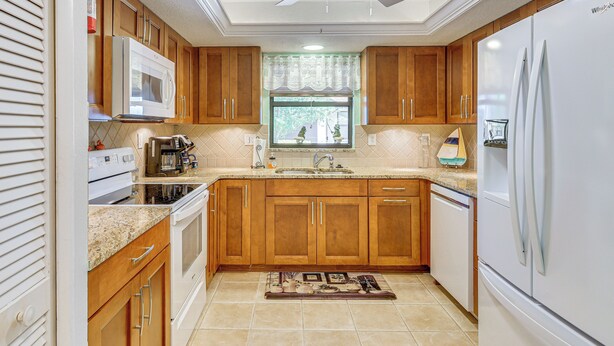 A kitchen with wooden cabinets, a white refrigerator, a microwave, and a ceiling fan. - 5 Mi to Fort Myers Beach: Home w/ Large Yard! (Fort Myers)