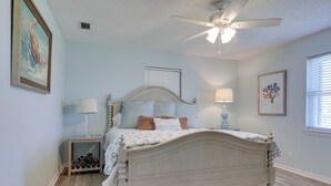 A bedroom with a bed, two bedside tables, a ceiling fan, and a window with blinds. - 1 Block to Gulf: Dauphin Island Retreat w/ Views (Dauphin Island)