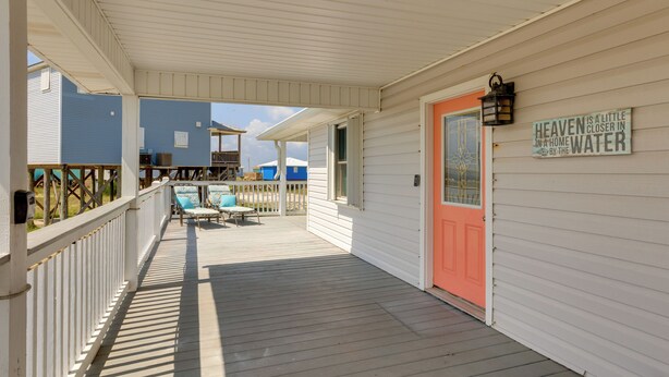 A covered porch with a wooden deck, a red door, and a sign that reads "Heaven is a little closer in a home by the water." - 1 Block to Gulf: Dauphin Island Retreat w/ Views (Dauphin Island)