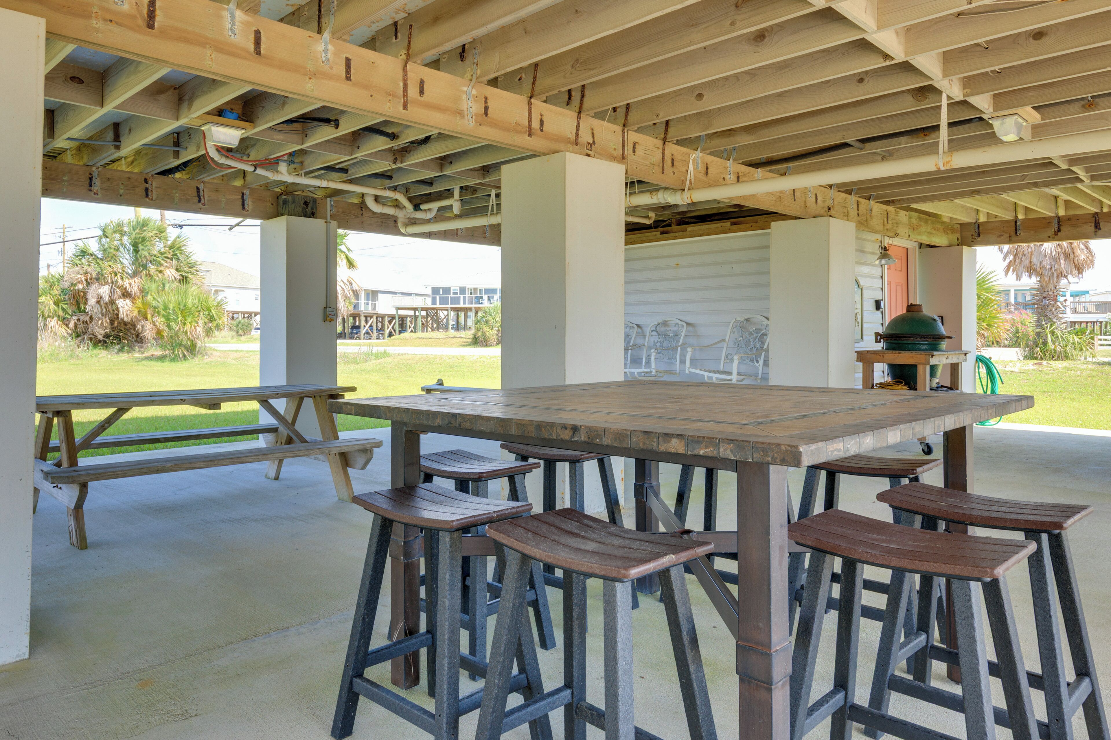 An outdoor covered patio with a wooden table and bar stools, concrete floor, and visible structural beams.