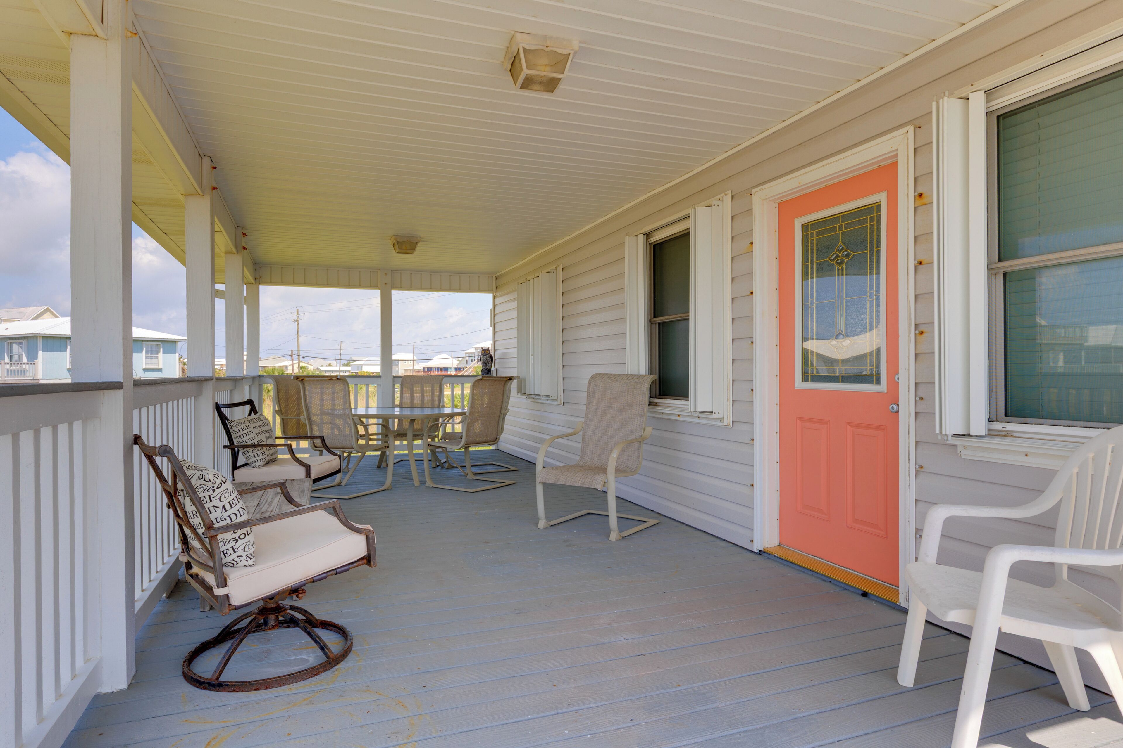 A porch with white railings, rocking chairs, and a bright pink door.