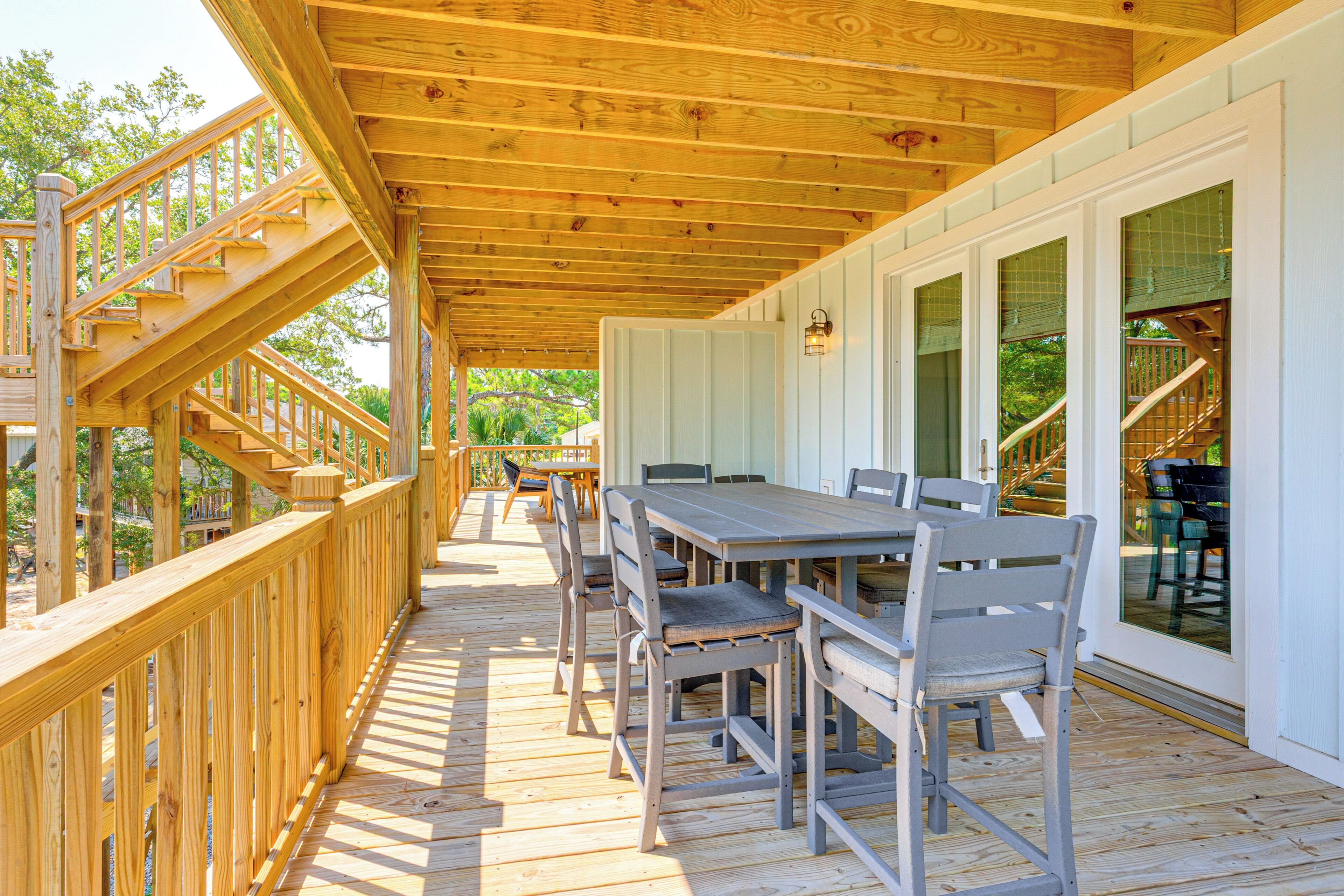 Una terraza cubierta al aire libre con una escalera de madera, una mesa de comedor con sillas y ventanas grandes.