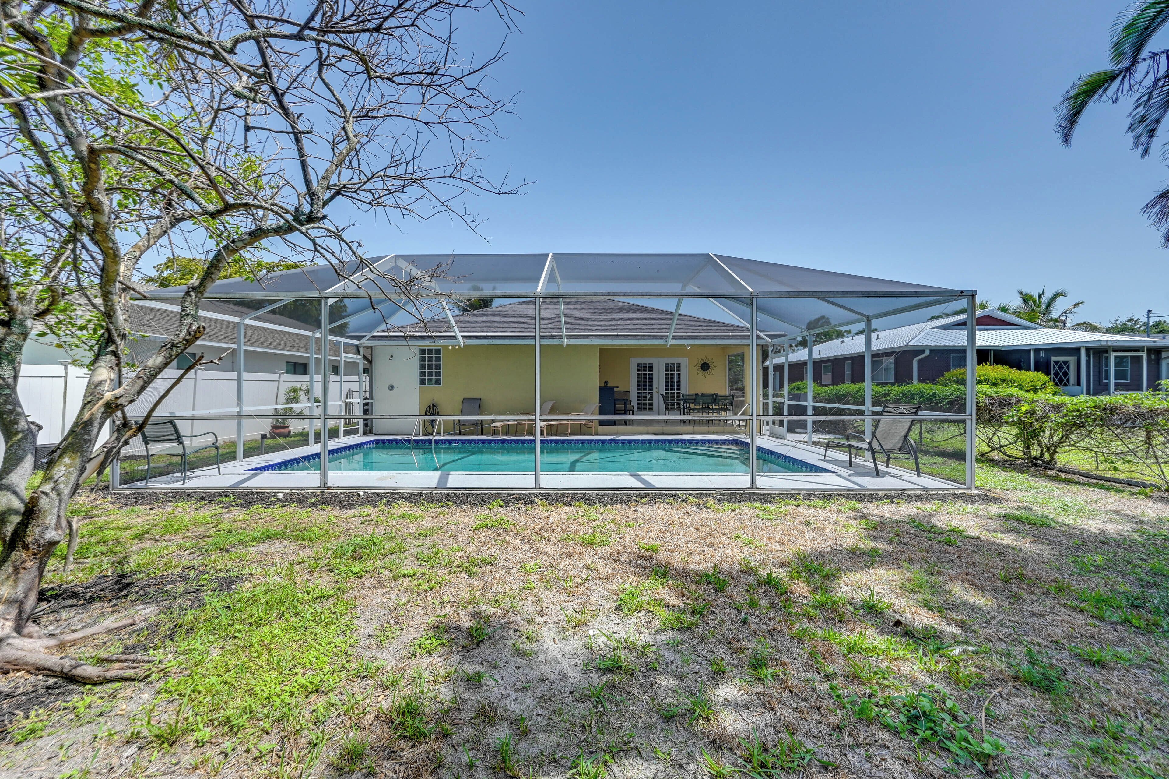 Ein Haus mit überdachtem Pool, einem Rasen und einem Baum.