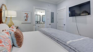 Ett sovrum med en säng, en tv som är monterad på väggen, en lampa och en inramad tavla på väggen.
