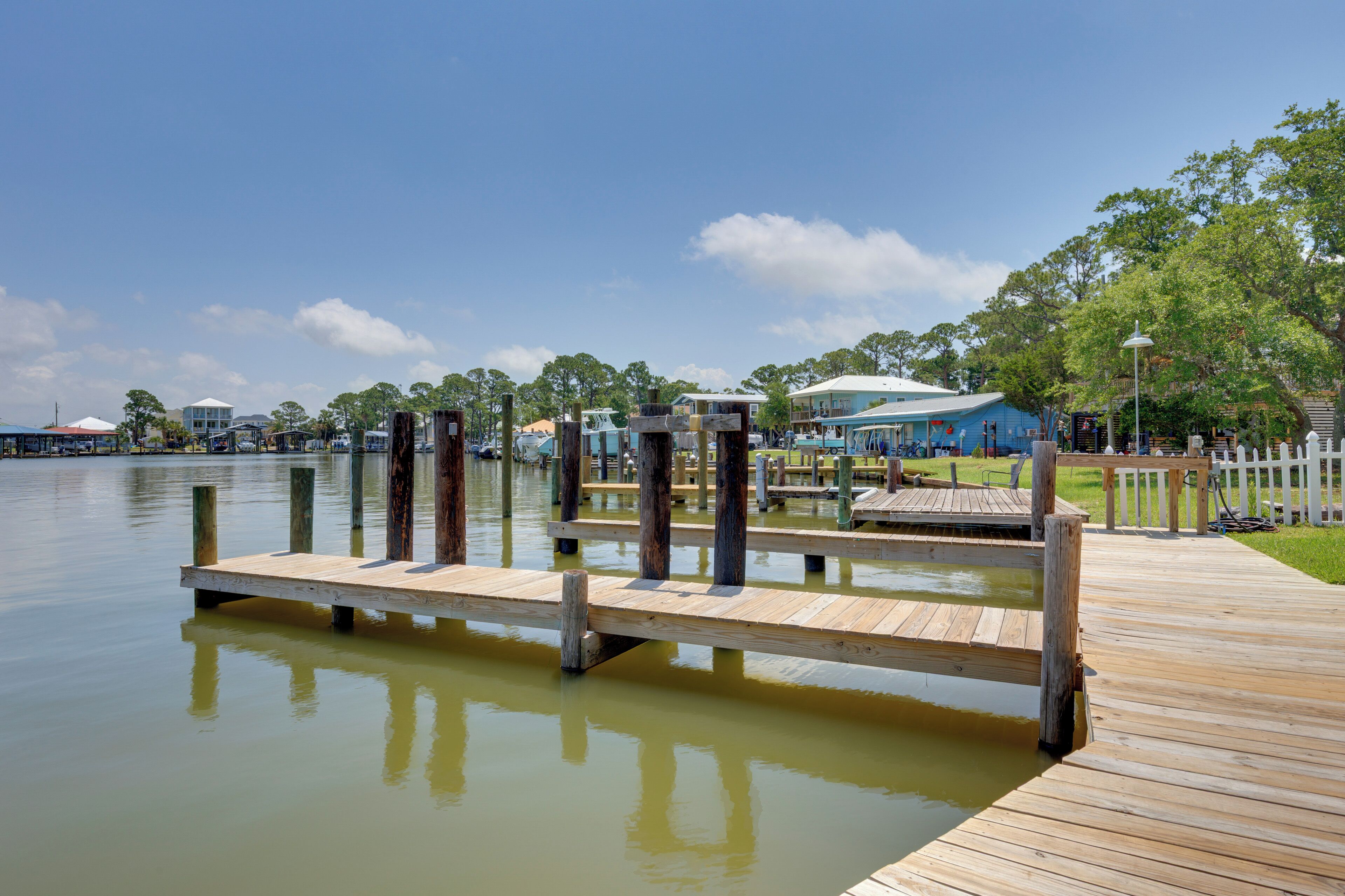 A wooden dock extending into a calm body of water, surrounded by a wooden fence and a grassy area with a gazebo.