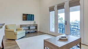A living room with a sofa, a coffee table, a TV, and a view of the outside balcony. - Bayfront Gem Near Fishing in Dauphin Island (Dauphin Island)