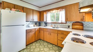 A compact kitchen with wooden cabinets, a white refrigerator, a stove, and a window with curtains. - Fisher's Retreat: Hayward Home, Near ATV Trails! (Hayward)