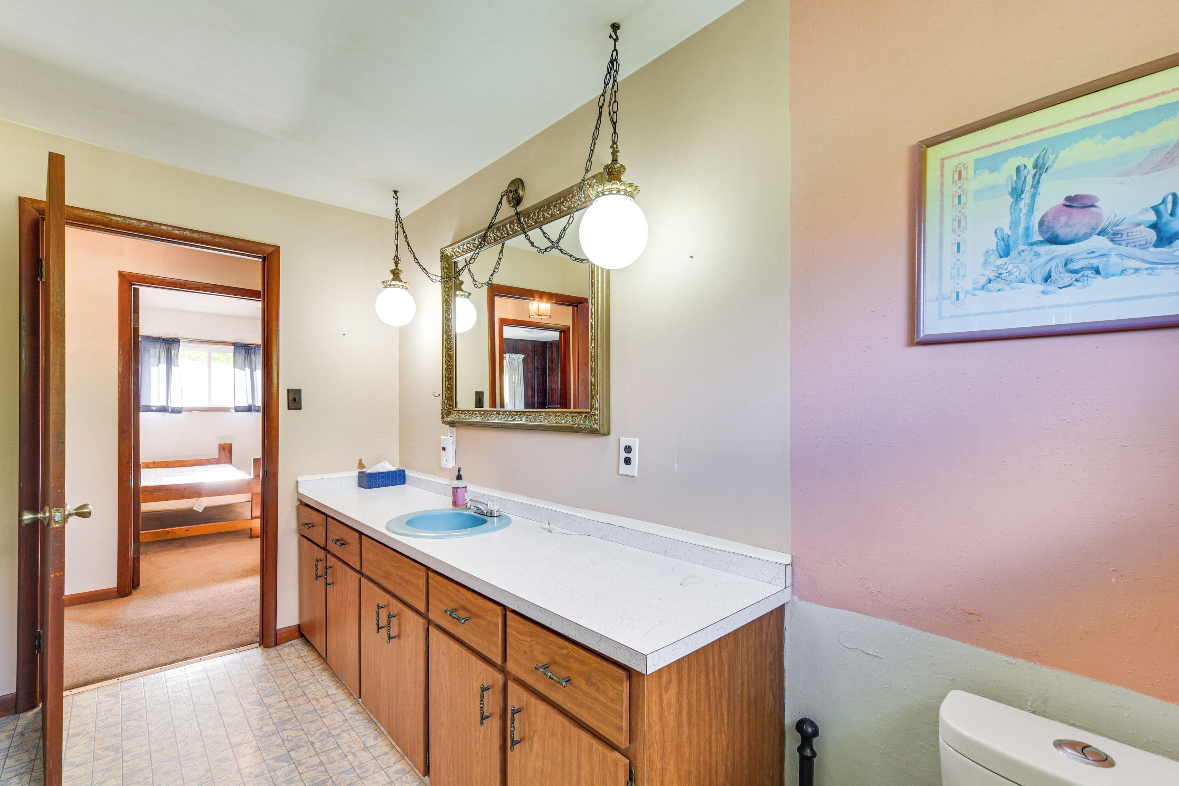 A bathroom with a wooden vanity, a blue sink, and a large mirror with a decorative frame.
