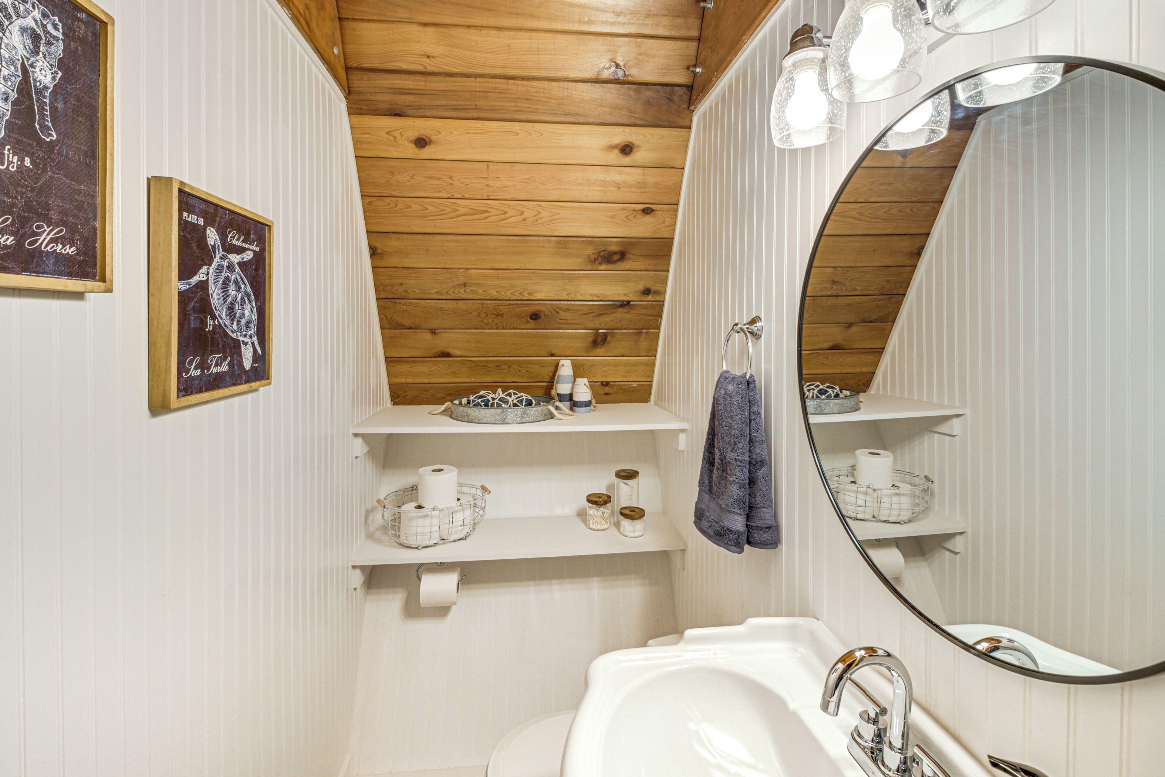 A bathroom with a wooden ceiling, a white sink, a large mirror, and shelves with toiletries.