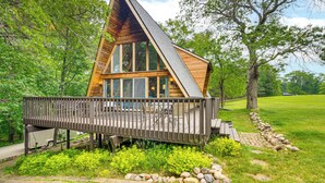 A wooden cabin with a sloped roof, large windows, and a deck. - Canal Across Street: Family Cabin in Breezy Point! (Pequot Lakes)