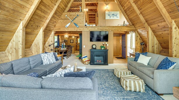 A spacious loft with high ceilings, wooden beams, a fireplace, and a cozy seating area with sofas and a rug. - Canal Across Street: Family Cabin in Breezy Point! (Pequot Lakes)