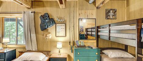 Una cabaña de madera con literas, un aparador, un escritorio y una ventana con cortinas.