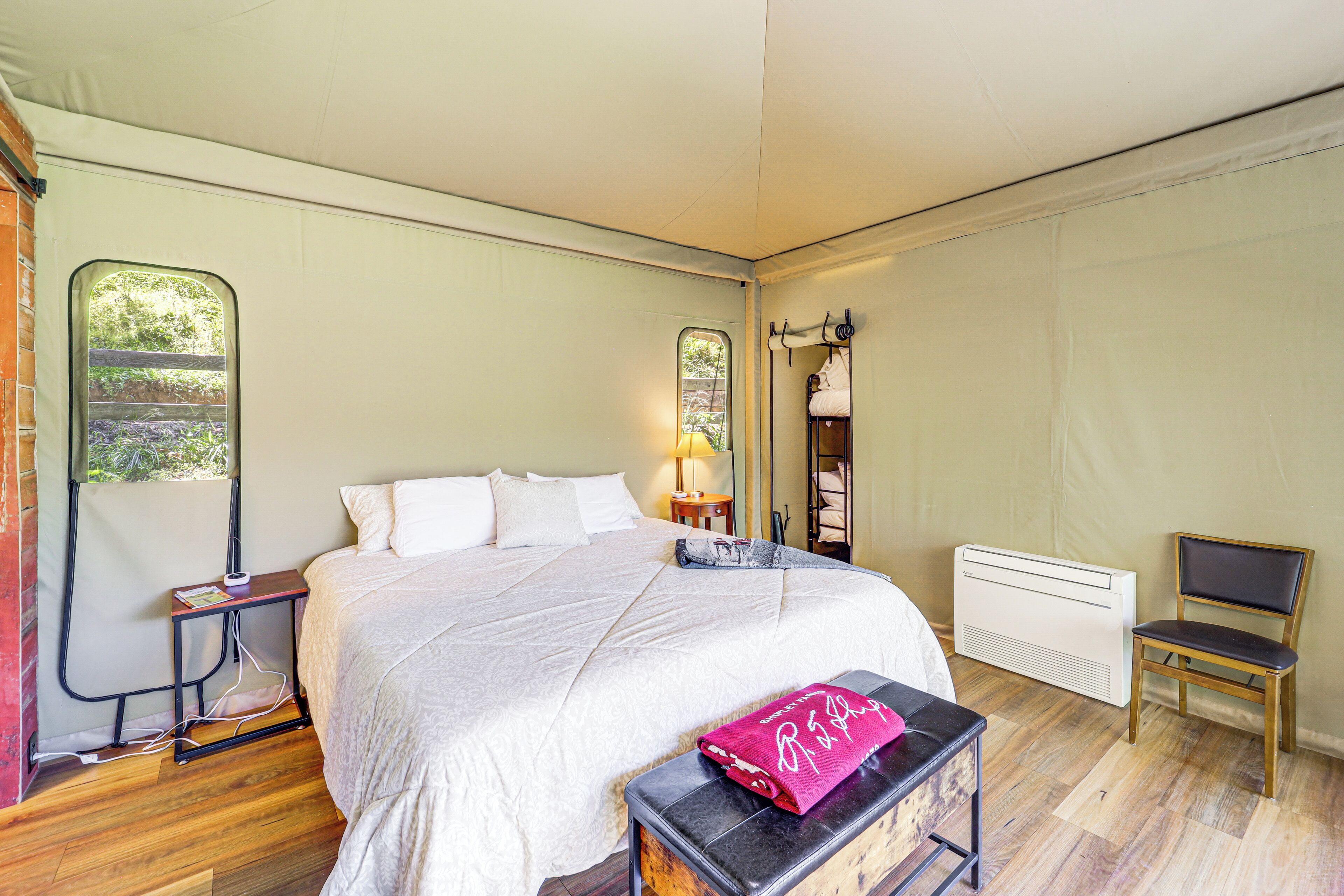 Una camera da letto con un letto grande, un comodino, una sedia, un termosifone e una finestra con vista sul verde.