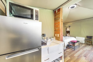 Habitación compacta con kitchenette, que incluye refrigerador, microondas y lavamanos. Tiene una cama con cabecera de madera, una mesita y una silla.