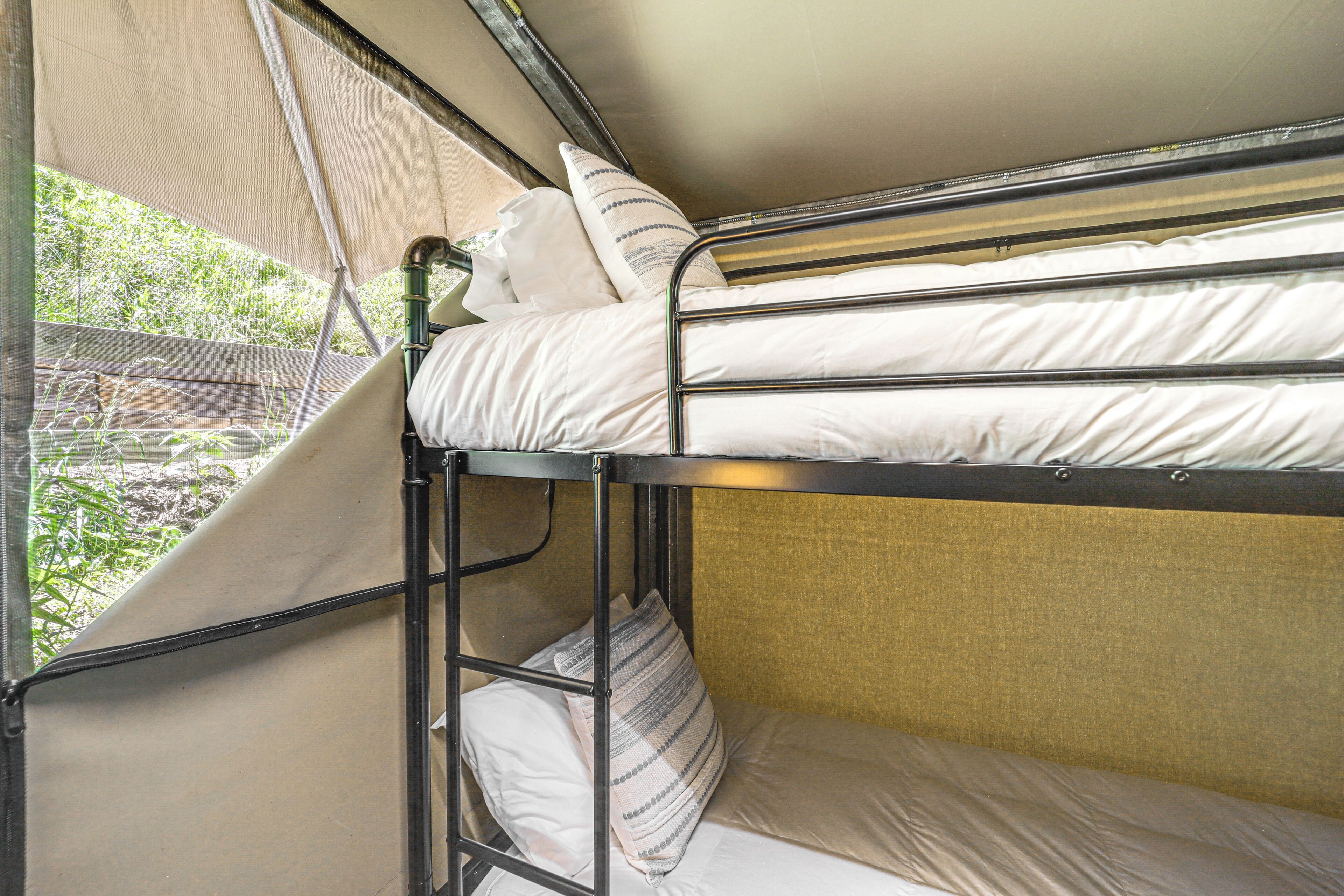 A bunk bed with two levels, a window with a view of greenery, and a canopy.