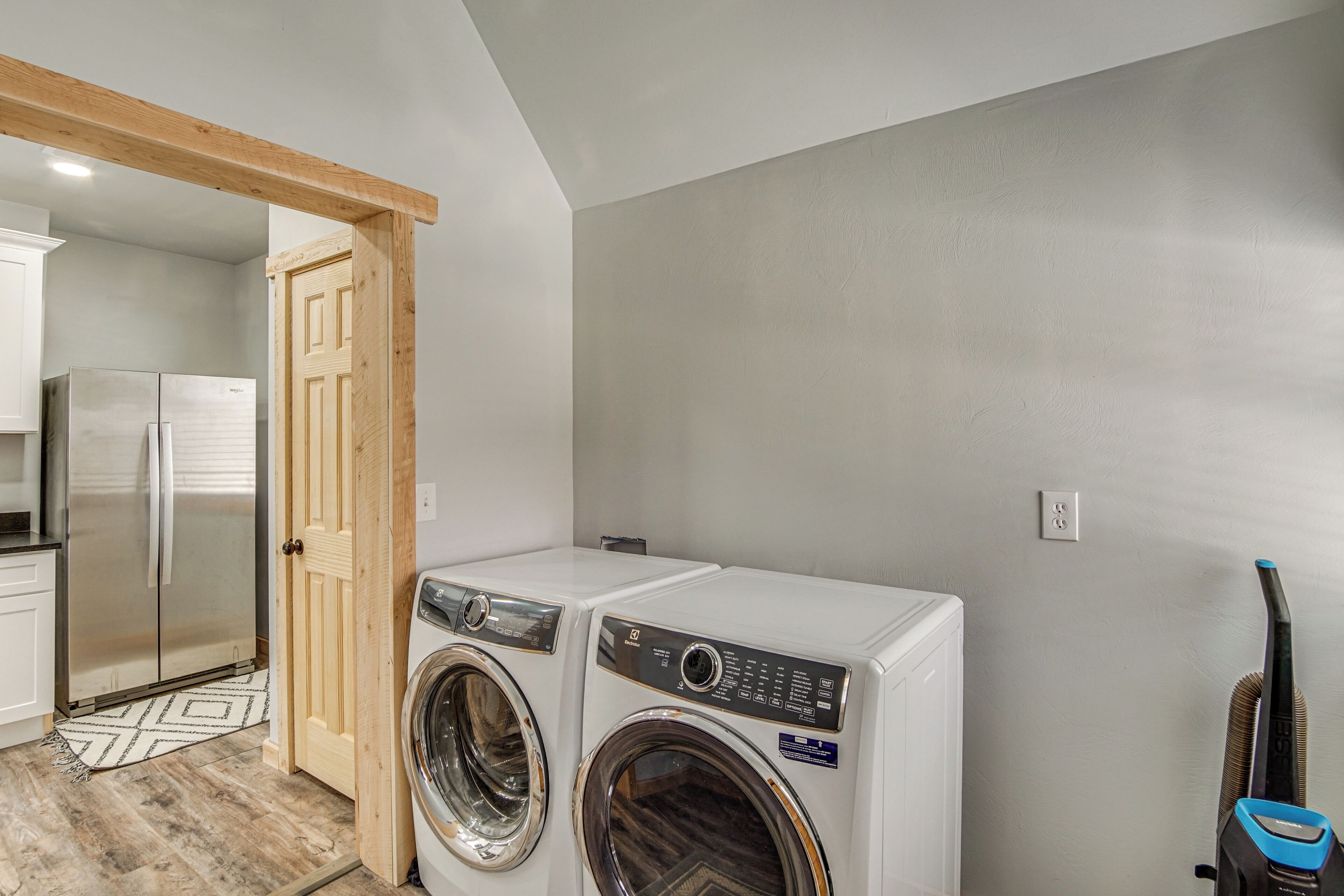 A laundry room with two front-loading washing machines, a wooden door, a refrigerator, and a vacuum cleaner.