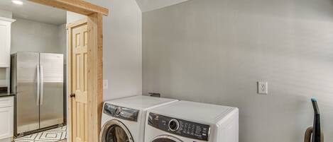 A laundry room with two front-loading washing machines, a wooden door, a refrigerator, and a vacuum cleaner.
