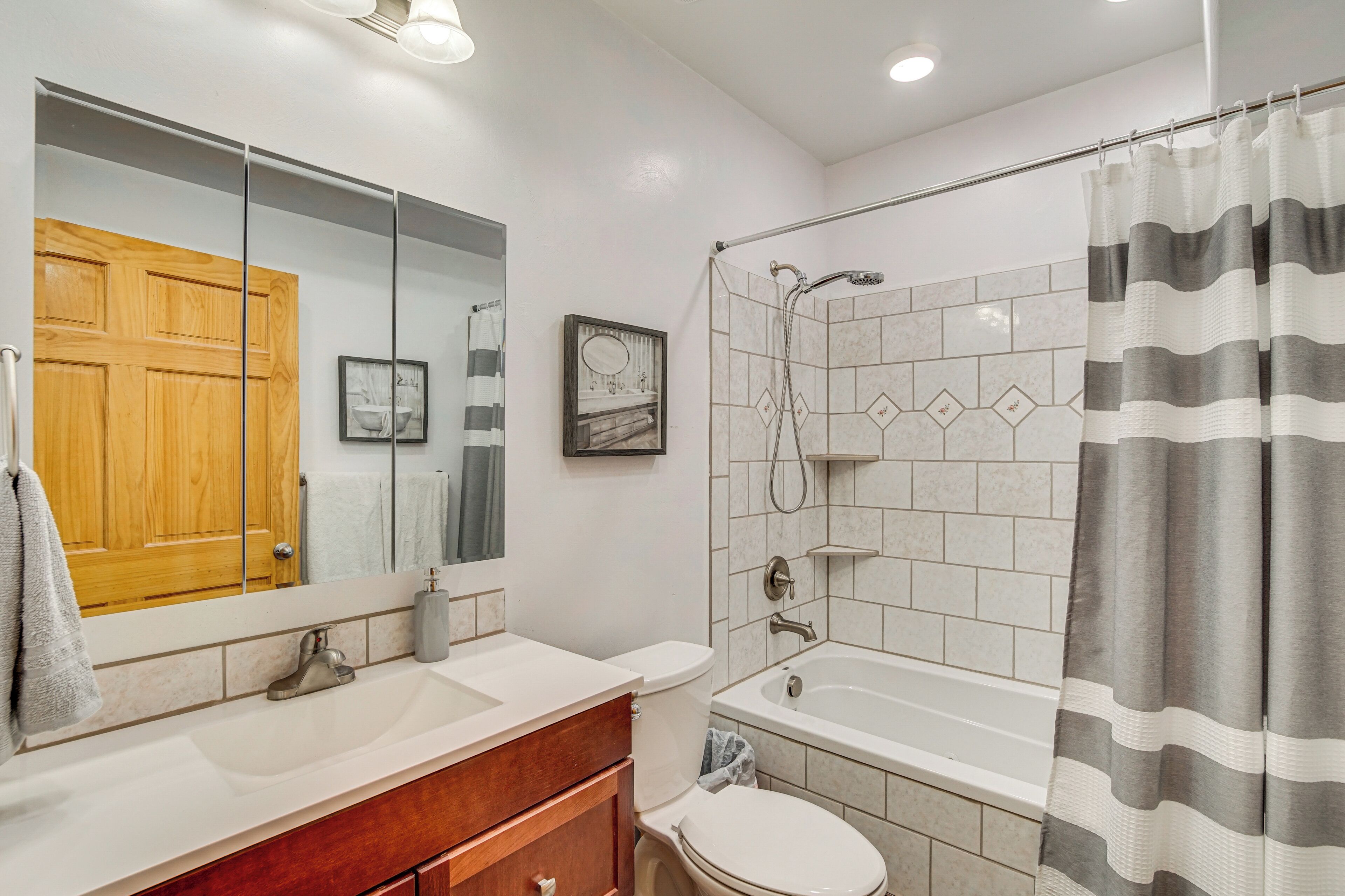 Baño con puerta de madera, espejo grande, lavabo blanco, inodoro y zona de ducha con cortina a rayas.