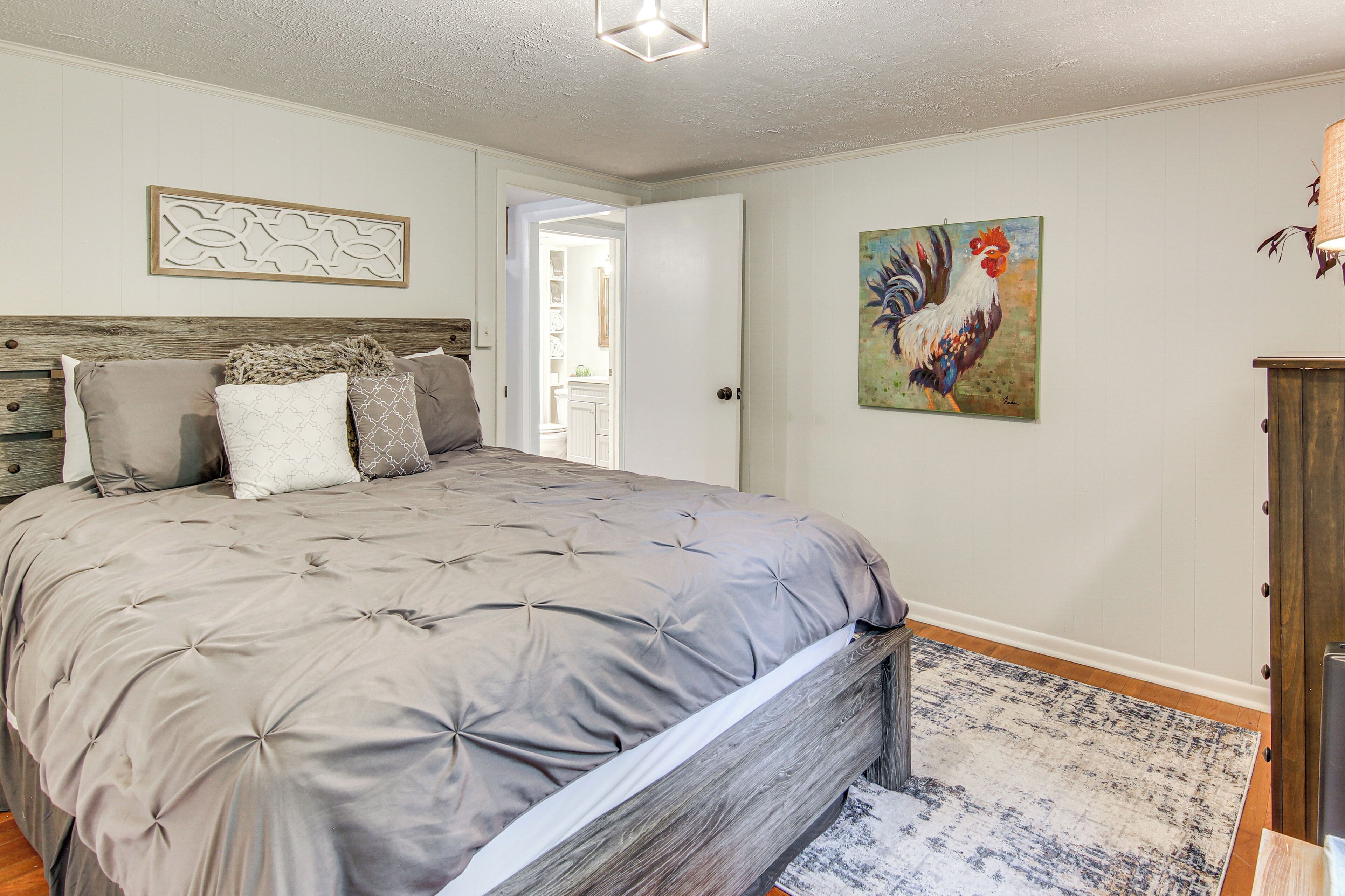 A bedroom with a large bed, a wooden headboard, a decorative wall piece, and a rooster painting.