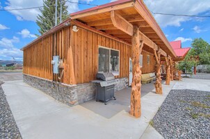 A wooden cabin with a stone foundation, a barbecue grill, and a covered outdoor area.