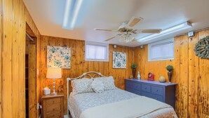 A bedroom with wooden walls, a bed with a floral bedspread, a nightstand with a lamp, a dresser, and a ceiling fan. - Group Getaway w/ Mtn Views: Home in Circleville! (Circleville)