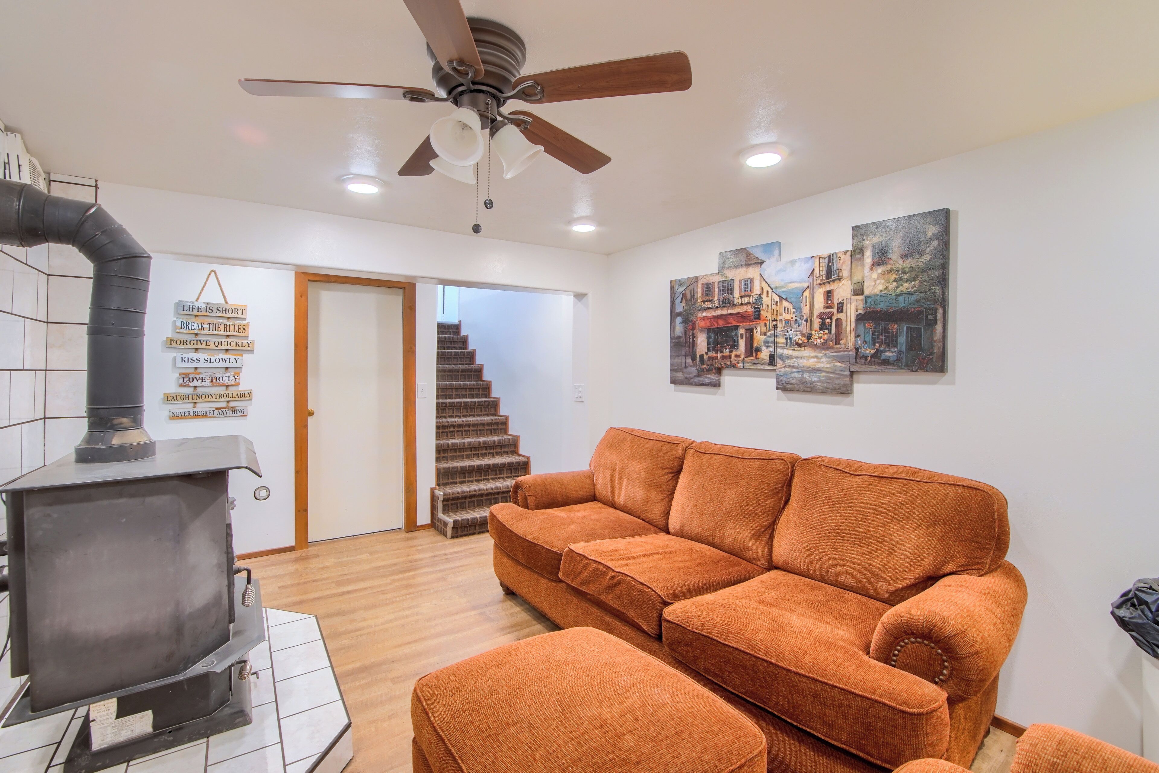 A living room with a sofa, a fireplace, a ceiling fan, and a staircase leading to another room.