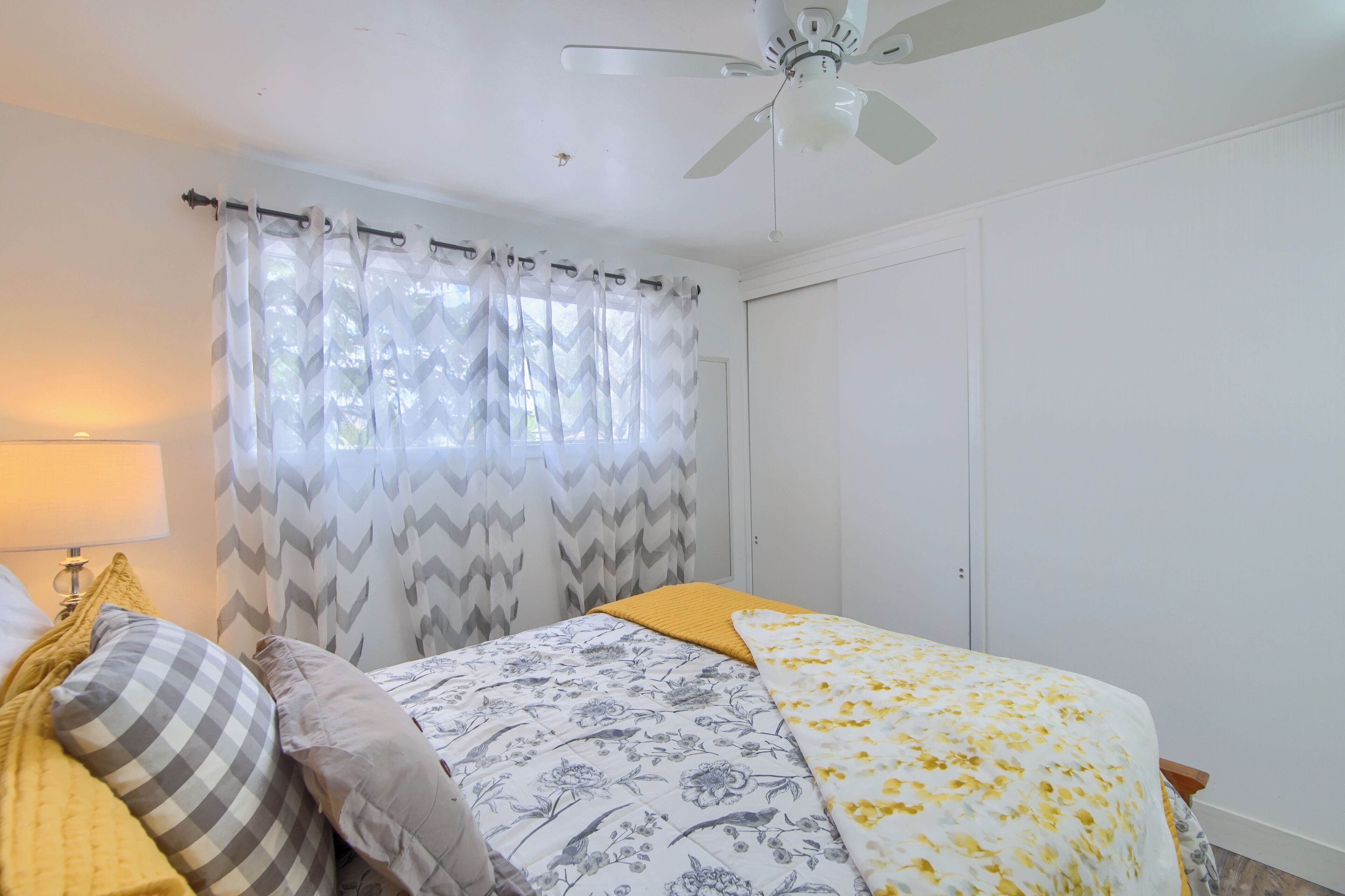 A bedroom with a bed, a ceiling fan, and a window with curtains.