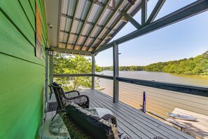 A covered deck with a view of a river, a chair, a table, and a kayak. - Private On-site Boat Dock: Cabin on Lake Jordan (Titus)