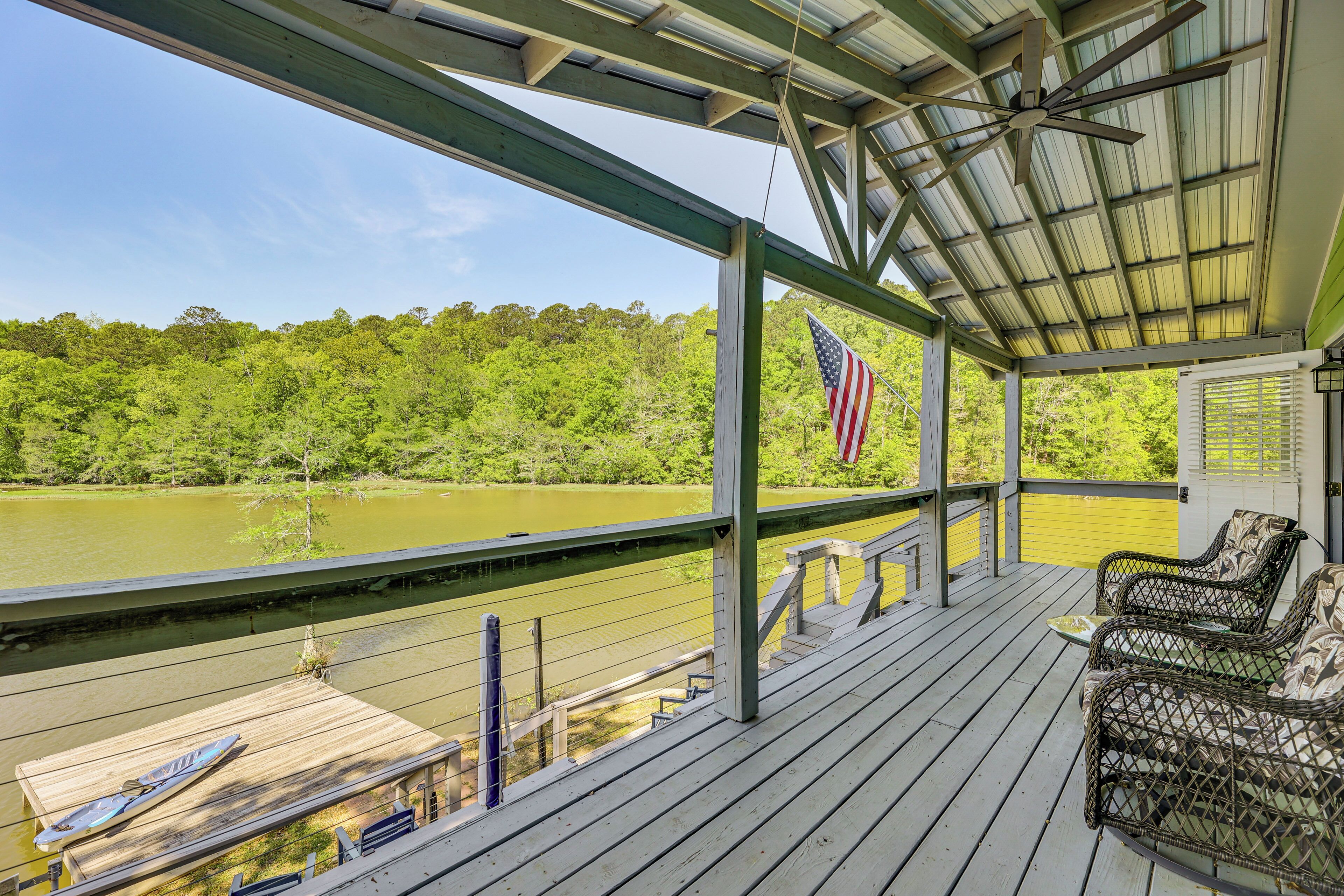 Een overdekt terras met uitzicht op een rivier, een Amerikaanse vlag en rieten meubilair.