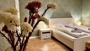 Un dormitorio con una cama blanca, una mesita de noche y un jarrón con flores.
