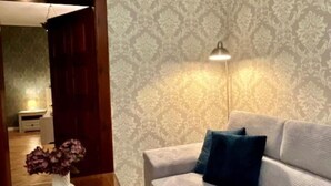 Una sala de estar con un papel tapiz estampado, un sofá con cojines y un jarrón con flores sobre una mesa.