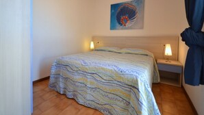 A bedroom with a bed, two bedside tables with lamps, a wooden ceiling, and a painting on the wall. - Feel at home in the center of Bibione (Bibione)