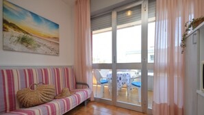 A room with a striped sofa, a painting of a beach scene, and a view of an outdoor area with a table and chairs. - Feel at home in the center of Bibione (Bibione)