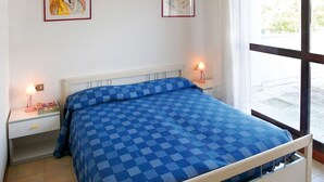 A bedroom with a checkered blue bedspread, white headboard, bedside tables with lamps, and framed artwork on the wall.