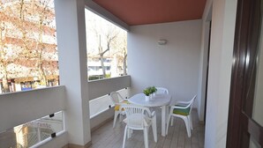 A balcony with a table and chairs, a potted plant, and a view of trees and buildings.