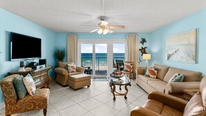 A living room with a TV, sofa, chairs, a glass coffee table, and a ceiling fan. - Gulf-view retreat w/ beach access (Panama City Beach)
