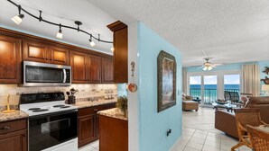 A kitchen with wooden cabinets, a microwave, and a stove. There is a dining area with a table and chairs, and a view of the ocean through large windows. - Gulf-view retreat w/ beach access (Panama City Beach)