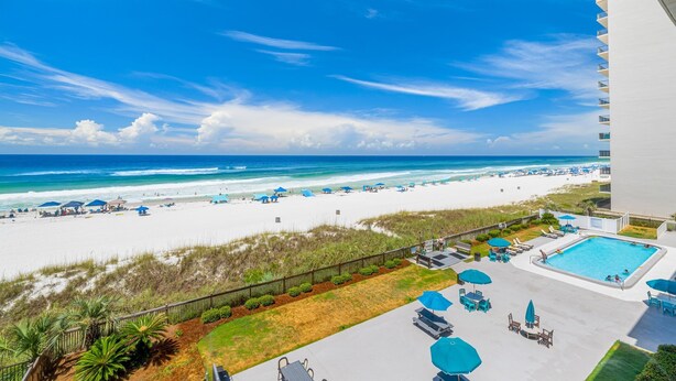 A beach view from a hotel balcony with a swimming pool and lounge chairs. - Gulf-view retreat w/ beach access (Panama City Beach)