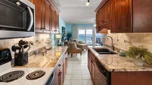 A kitchen with wooden cabinets, a large microwave, and a granite countertop. - Gulf-view retreat w/ beach access (Panama City Beach)