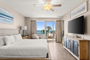 A bedroom with a large bed, a ceiling fan, a TV, and a view of the ocean. - Gulf-front condo w/ wraparound balcony & pool (Panama City Beach)