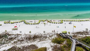Une plage avec une promenade en bois menant à l’eau, bordée de parasols verts et de chaises de plage.