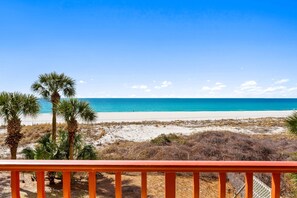 Vista a la playa desde un balcón con barandilla, palmeras y cielo despejado.