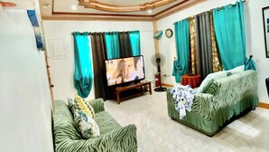 A spacious living room with a television, two green sofas, and a ceiling with a decorative design. - Len's Staycation 3bdr-2br-downstairs ,netflix&wifi (Davao)