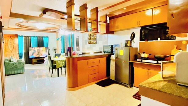 A spacious kitchen with a central island, a dining area with a sofa, and a living room with a television. - Len's Staycation 3bdr-2br-downstairs ,netflix&wifi (Davao)
