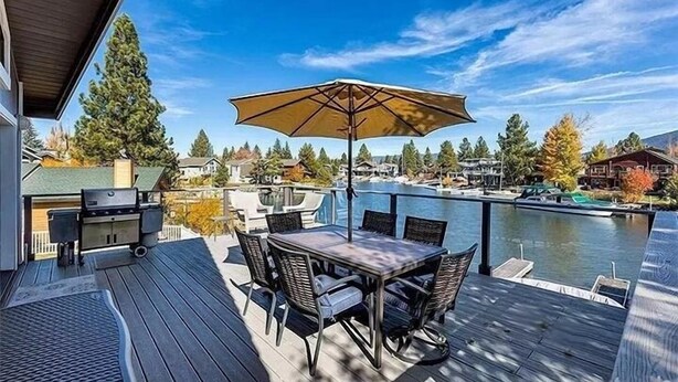 Una terrazza con tavolo e sedie, un barbecue e vista su un lago con barche.