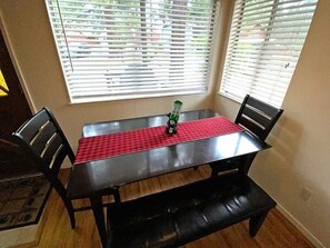 A dining table with a red checkered tablecloth, two chairs, and a bench.