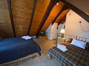 A cozy attic bedroom with a wooden ceiling, a bed, a nightstand, and a lamp.