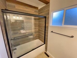 A glass-enclosed shower with a towel rack and a window above it.