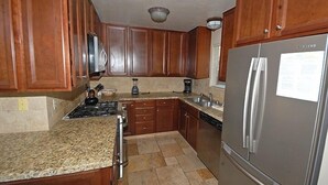 Eine Küche mit Holzausstattung, einem Edelstahlkühlschrank, Granitarbeitsplatten, einem Herd und einer Kaffeemaschine.