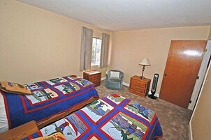 Un dormitorio con dos camas, una silla, una mesita de noche, una lámpara y una puerta.